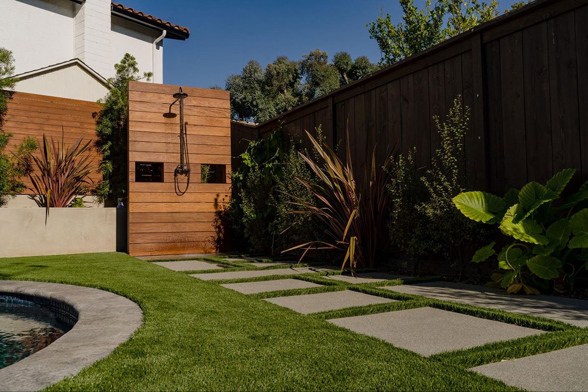 artificial turf in a backyard with an outdoor shower and pool