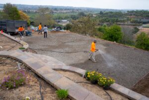 A few men working on an artificial grass installation. Most of the men are unloading the truck and one is watering the base layer. 