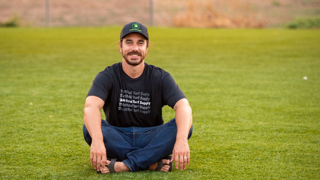 a photo of an Artificial Turf Supply employee grinning as he sits on new turf