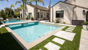 a photo of pavers in artificial grass next to a beautiful luxury pool on a sunny day