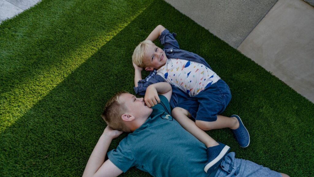 a photo of two boys lounging comfortably on soft turf