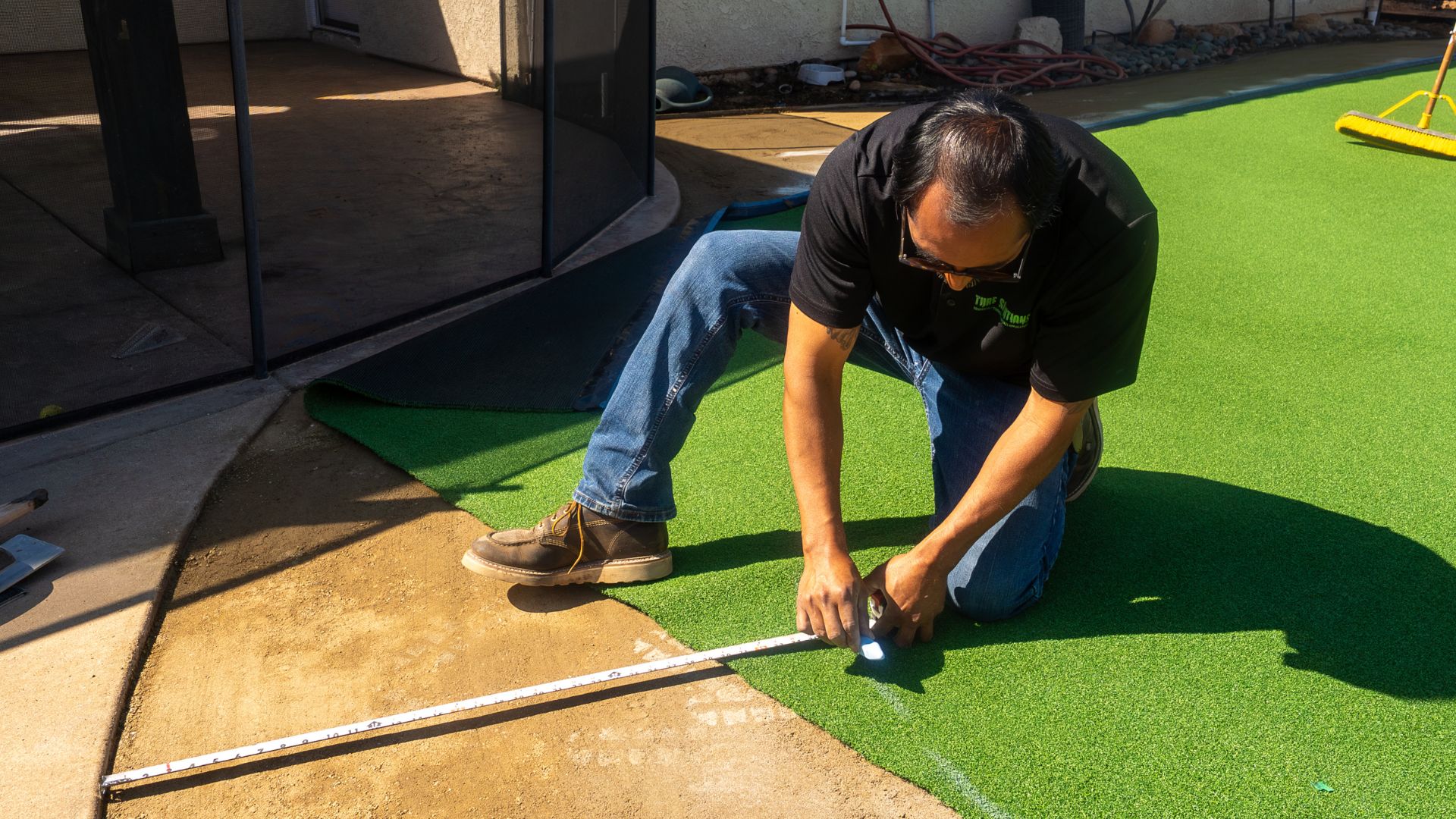 a photo of a professional synthetic grass installer carefully measuring for a cut