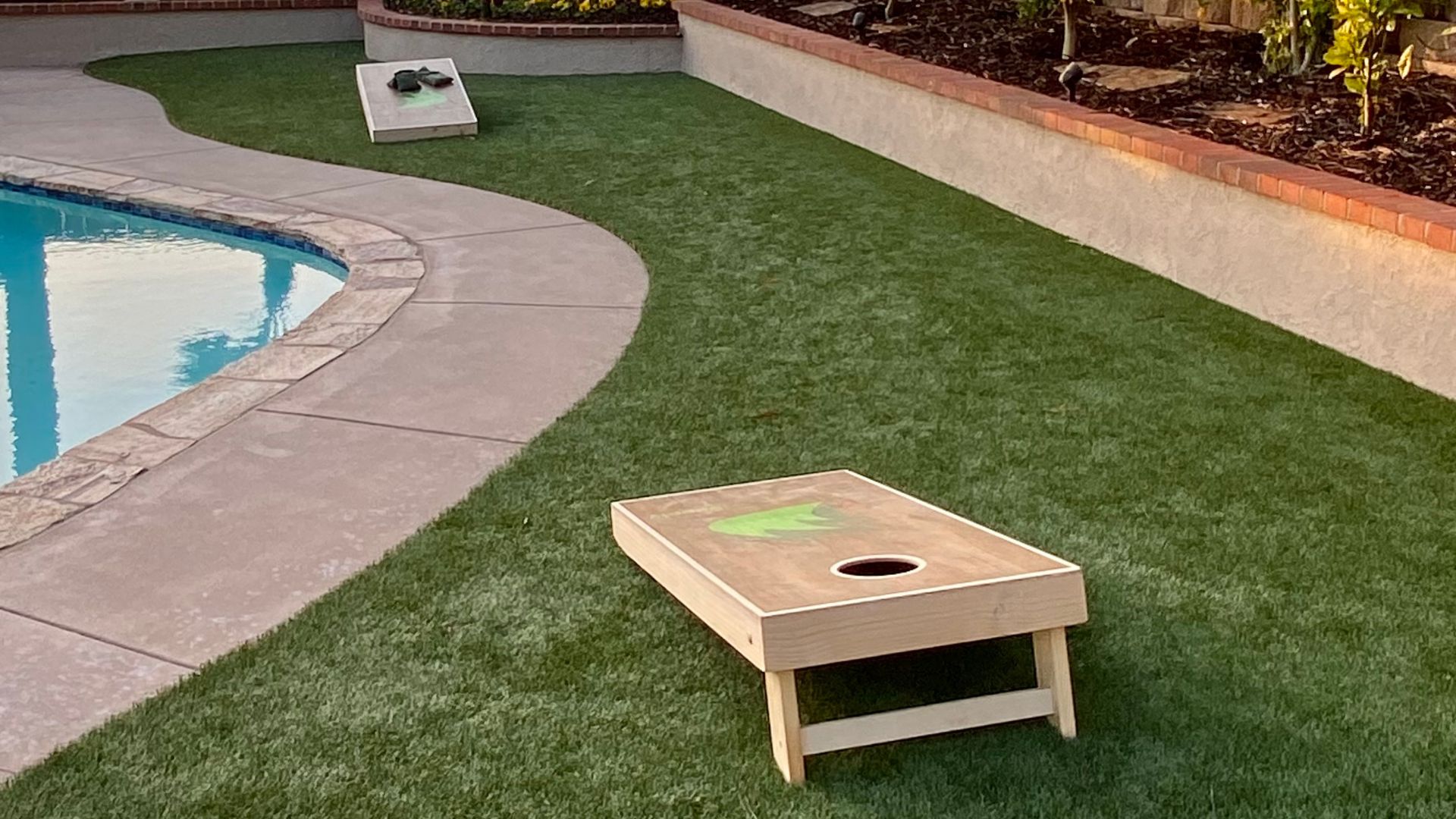 a residential backyard lawn installed by Artificial Turf Supply with a pool and corn hole game